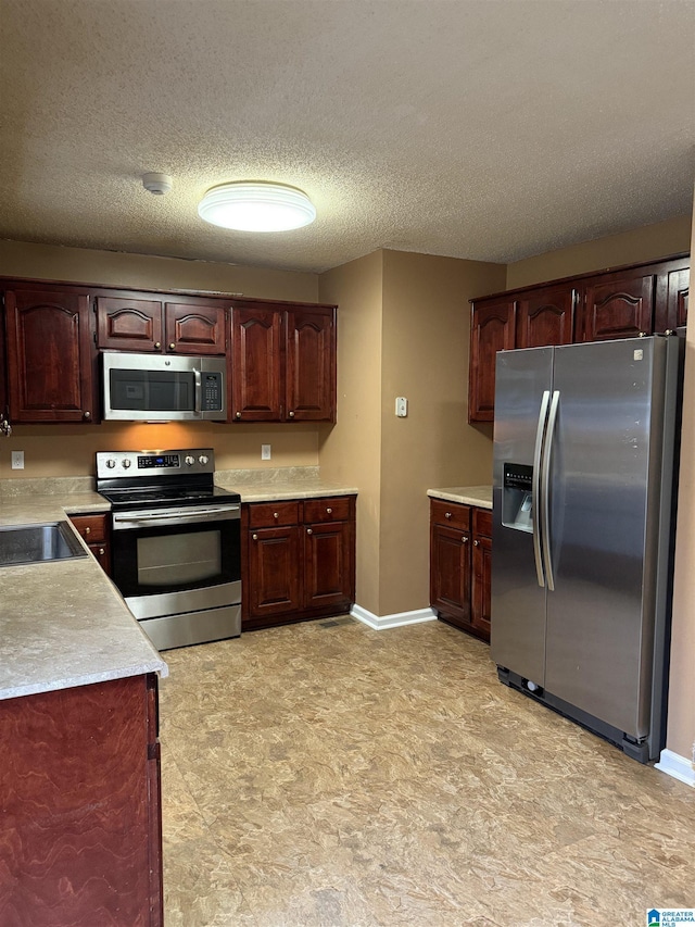 kitchen with a textured ceiling, stainless steel appliances, a sink, baseboards, and light countertops