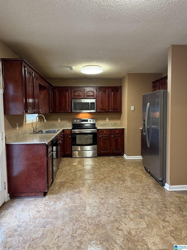 kitchen featuring baseboards, appliances with stainless steel finishes, light countertops, a textured ceiling, and a sink