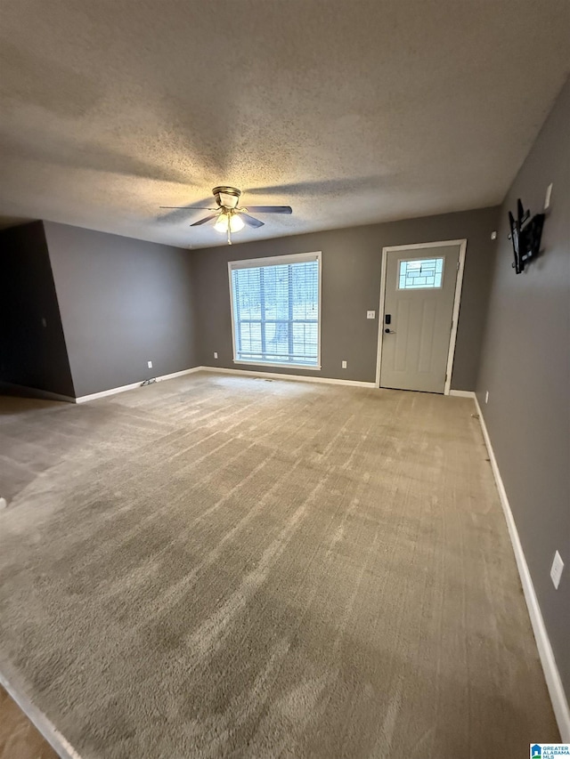 unfurnished living room with ceiling fan, a textured ceiling, and baseboards