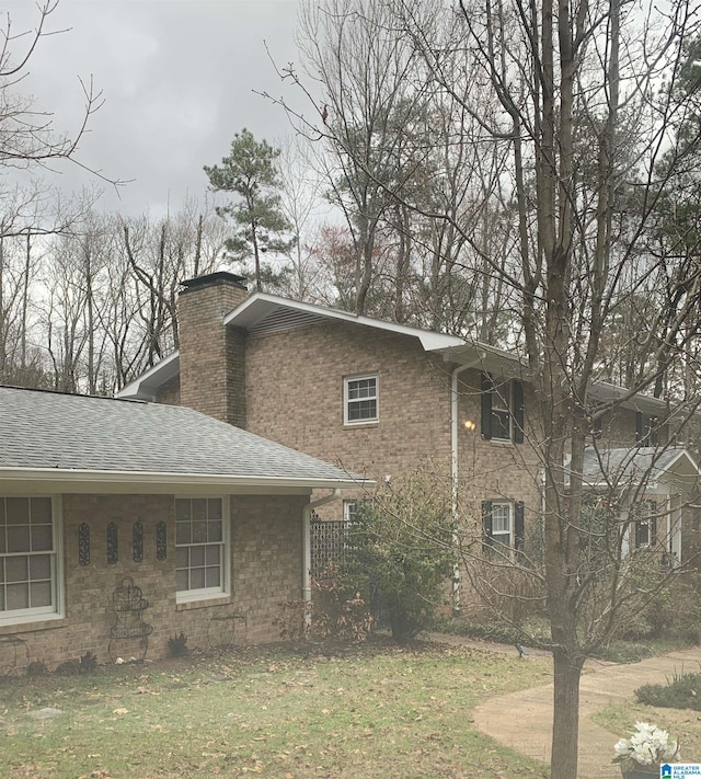 view of home's exterior featuring a lawn, a chimney, roof with shingles, central AC, and brick siding