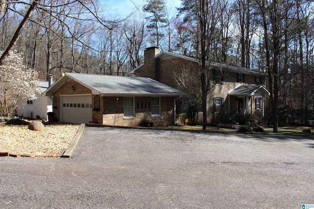 view of front facade with aphalt driveway, a chimney, and an attached garage