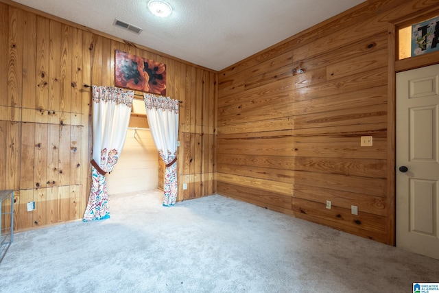 carpeted empty room featuring a textured ceiling and wood walls