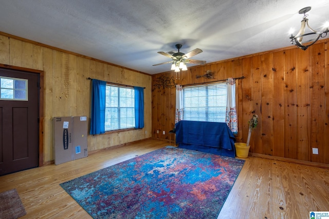 entryway with ceiling fan with notable chandelier, wood-type flooring, ornamental molding, and wooden walls