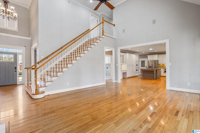 unfurnished living room with stairway, ornamental molding, light wood-style floors, baseboards, and ceiling fan with notable chandelier