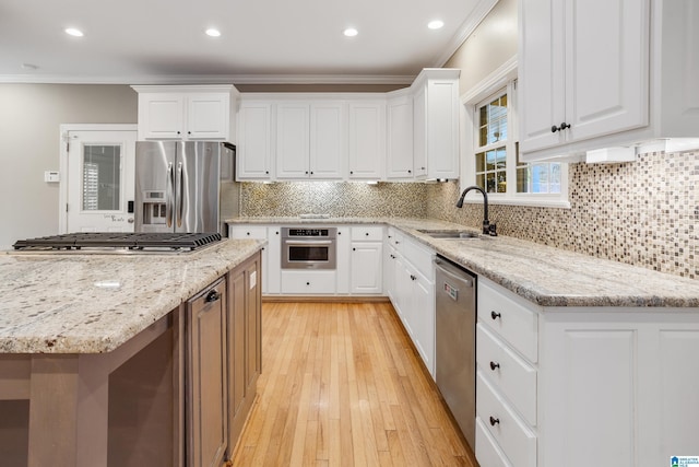 kitchen featuring appliances with stainless steel finishes, light wood-style floors, ornamental molding, white cabinets, and a sink