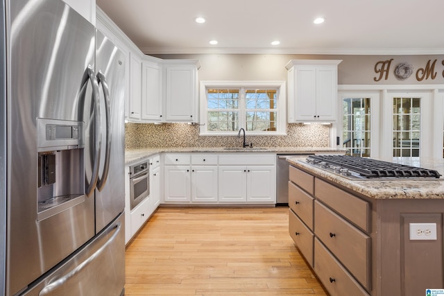 kitchen with crown molding, backsplash, light wood-style flooring, appliances with stainless steel finishes, and a sink