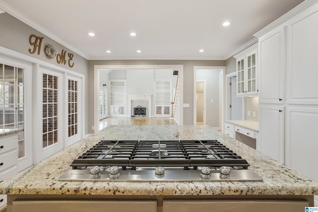 kitchen featuring ornamental molding, a fireplace, stainless steel gas stovetop, and white cabinetry