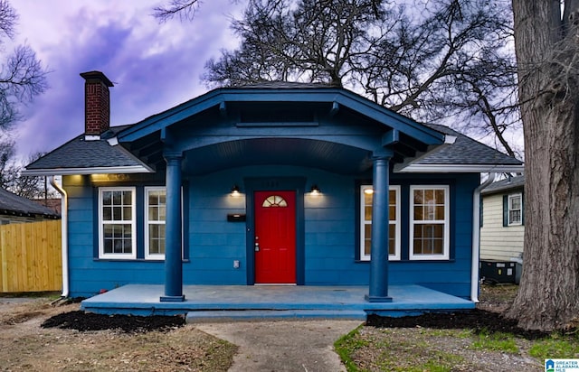 bungalow-style home with a shingled roof, a chimney, fence, and a porch