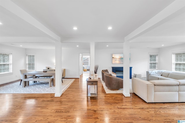 living room featuring light wood-type flooring, a glass covered fireplace, beam ceiling, and recessed lighting