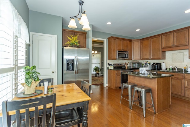 kitchen featuring pendant lighting, dark stone countertops, an inviting chandelier, stainless steel appliances, and a center island