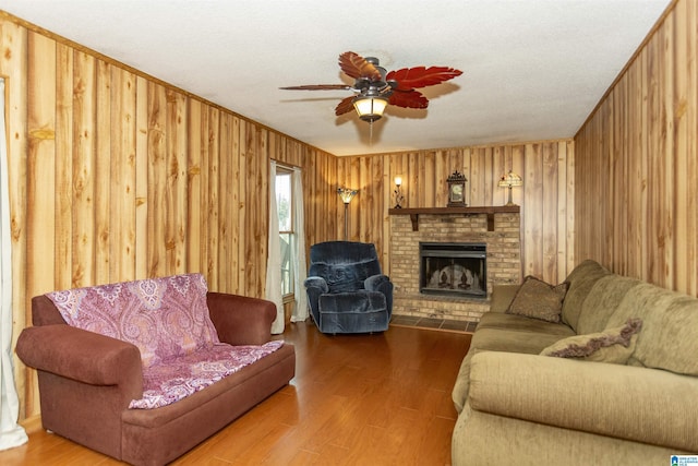 living room with hardwood / wood-style flooring, ceiling fan, wooden walls, and a fireplace