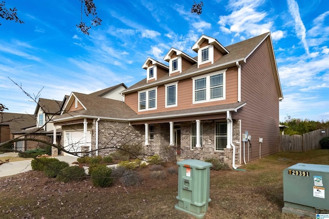 view of front facade with brick siding, roof with shingles, an attached garage, fence, and driveway