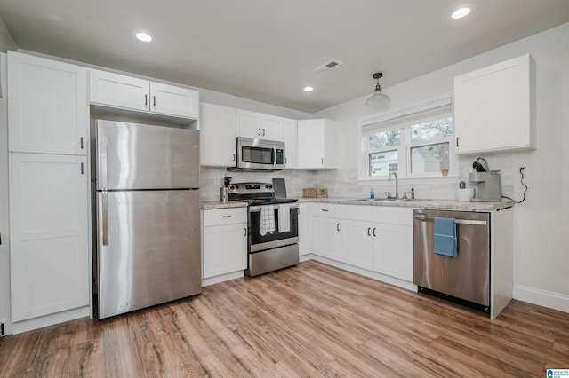 kitchen featuring sink, hanging light fixtures, stainless steel appliances, decorative backsplash, and white cabinets