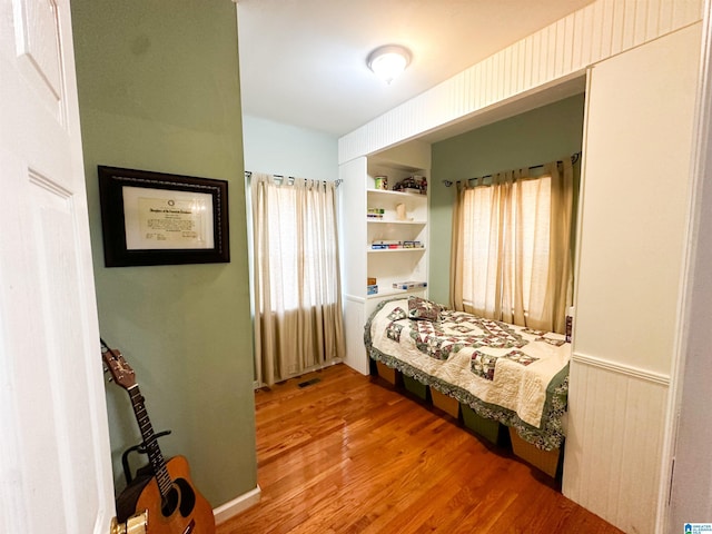 bedroom featuring a wainscoted wall, multiple windows, wood finished floors, and visible vents