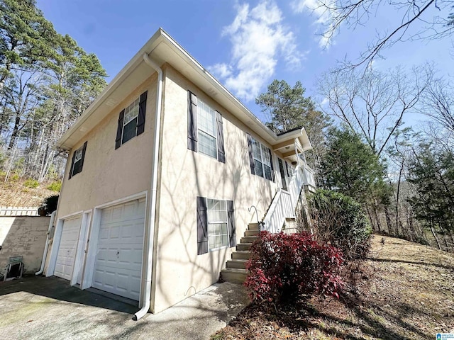 view of side of home with stairs, an attached garage, and stucco siding