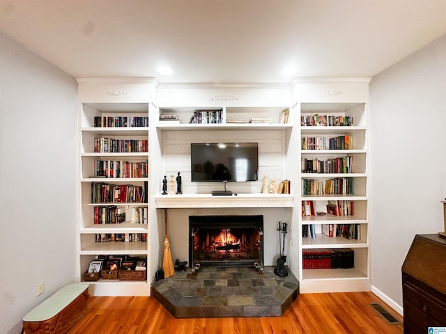 living area with a warm lit fireplace, wood finished floors, and visible vents