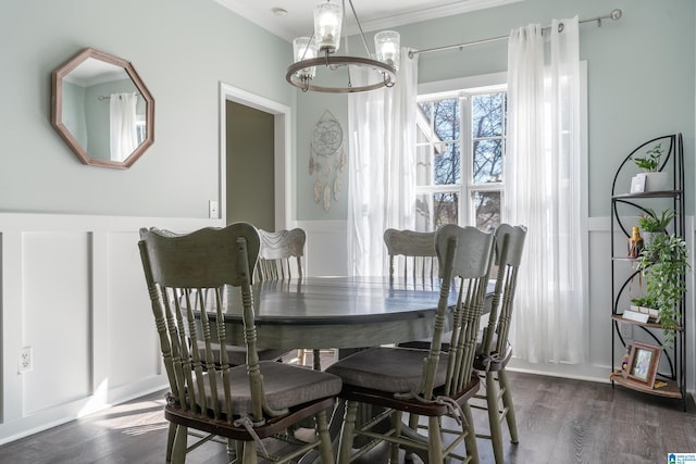 dining area with a wainscoted wall, dark wood-style flooring, an inviting chandelier, crown molding, and a decorative wall