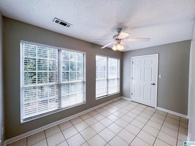 empty room with a textured ceiling, ceiling fan, and light tile patterned flooring