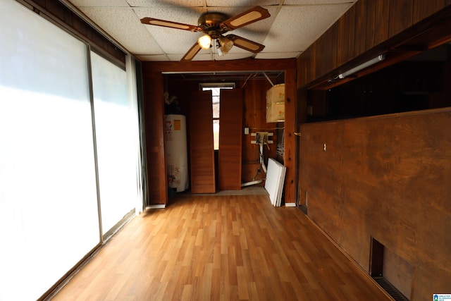 interior space featuring gas water heater, a paneled ceiling, wood walls, ceiling fan, and light hardwood / wood-style flooring