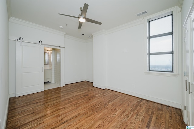 unfurnished bedroom featuring hardwood / wood-style flooring, crown molding, connected bathroom, and a barn door