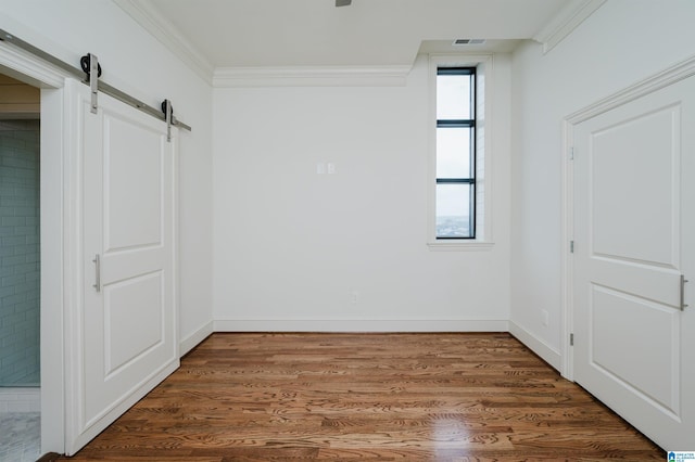 unfurnished room with crown molding, dark hardwood / wood-style flooring, and a barn door