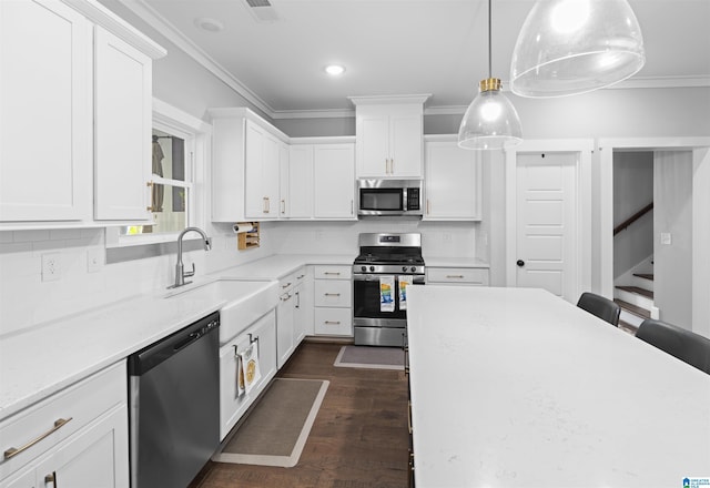 kitchen with appliances with stainless steel finishes, pendant lighting, sink, white cabinets, and ornamental molding