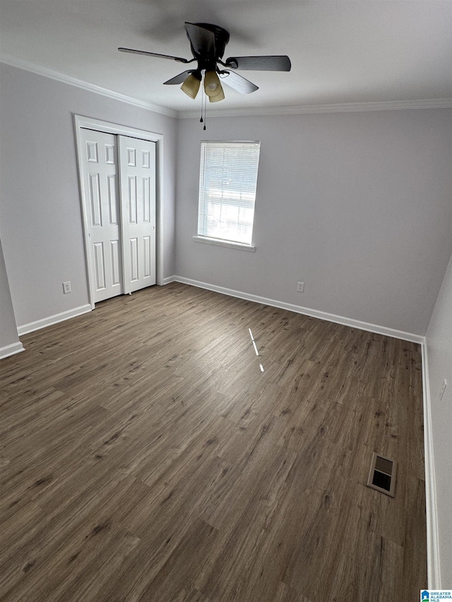 unfurnished bedroom featuring crown molding, ceiling fan, dark wood-type flooring, and a closet