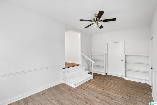 spare room featuring stairway, wainscoting, wood finished floors, and a ceiling fan