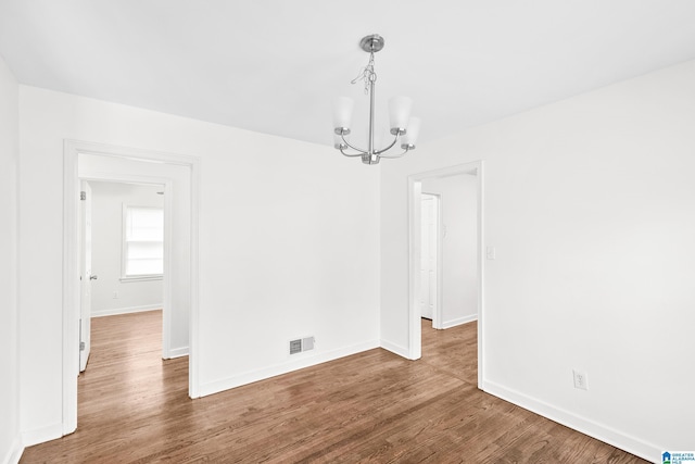 unfurnished dining area with a chandelier, wood finished floors, visible vents, and baseboards