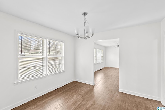 unfurnished dining area featuring ceiling fan with notable chandelier, baseboards, and wood finished floors