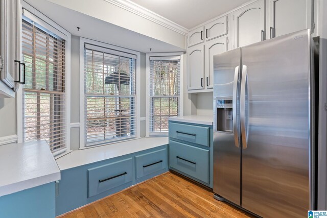 kitchen featuring white cabinetry, light countertops, ornamental molding, light wood-type flooring, and stainless steel refrigerator with ice dispenser