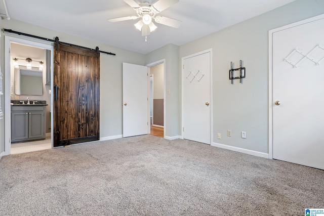 unfurnished bedroom with a barn door, light colored carpet, a sink, baseboards, and ensuite bath