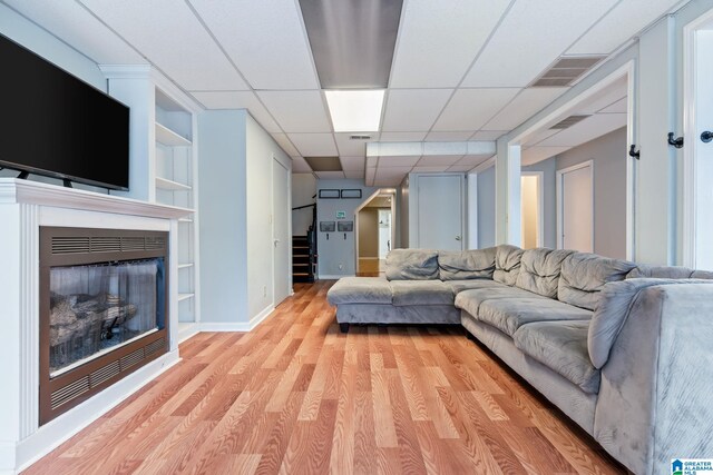 living area with visible vents, light wood-style flooring, a glass covered fireplace, baseboards, and stairs