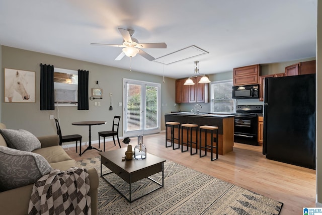 living room with a ceiling fan, light wood-type flooring, attic access, and baseboards