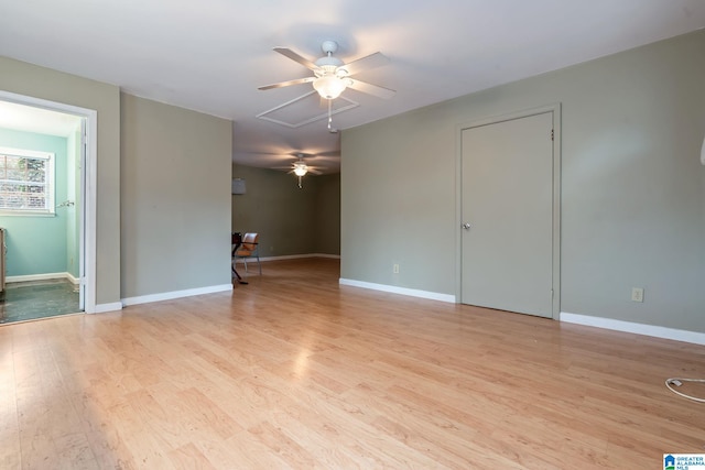 spare room with light wood finished floors, attic access, and baseboards