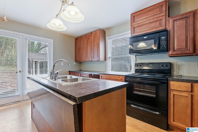 kitchen with a center island with sink, dark countertops, decorative light fixtures, black appliances, and a sink