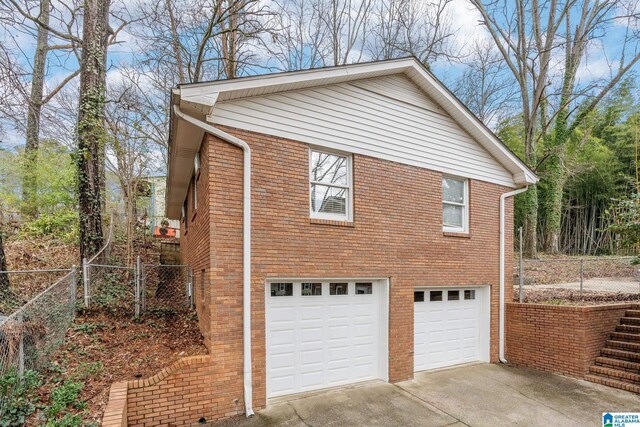 view of side of property with concrete driveway, brick siding, fence, and an attached garage