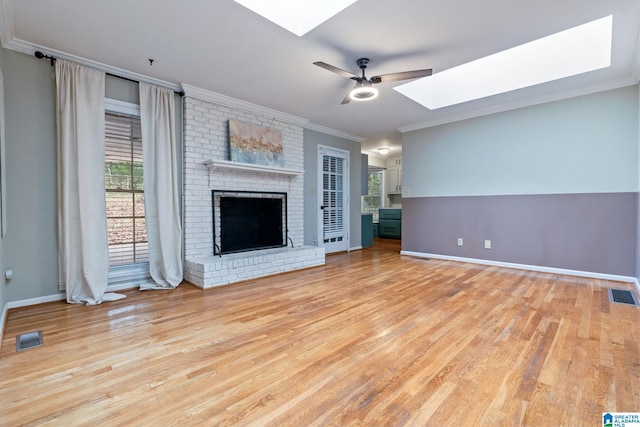 unfurnished living room featuring a ceiling fan, a skylight, visible vents, and crown molding