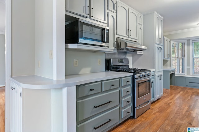 kitchen with crown molding, stainless steel appliances, light countertops, wood finished floors, and under cabinet range hood