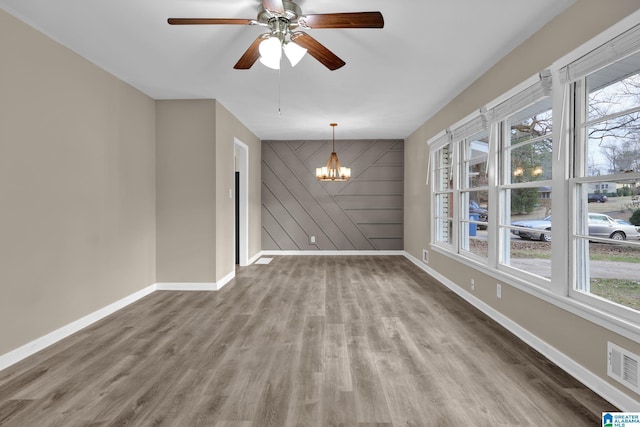 unfurnished dining area featuring hardwood / wood-style floors, ceiling fan with notable chandelier, plenty of natural light, and wood walls