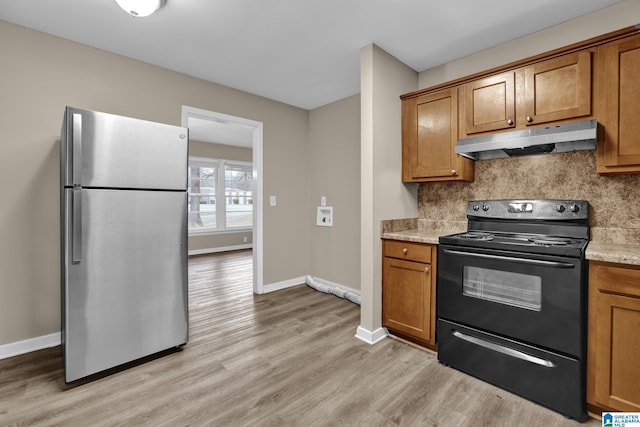 kitchen featuring tasteful backsplash, light stone counters, light hardwood / wood-style flooring, stainless steel fridge, and black range with electric stovetop