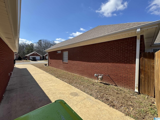 view of side of home with a patio area, brick siding, a shingled roof, and fence