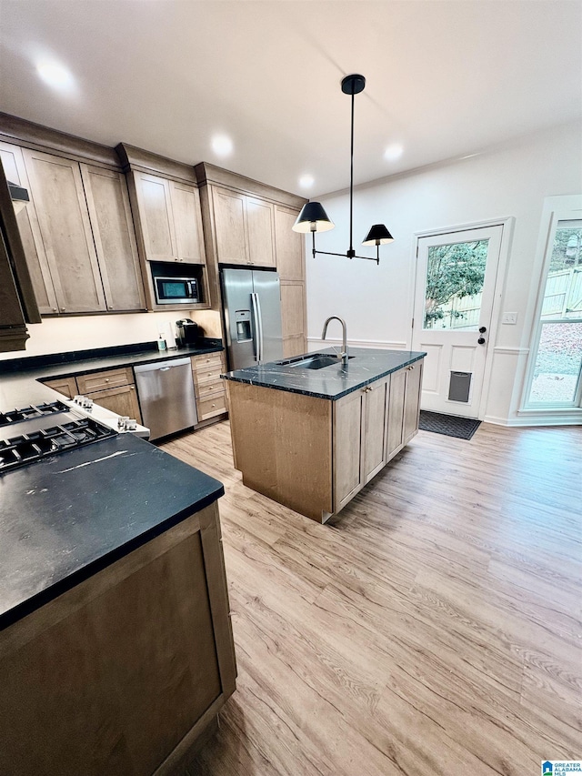 kitchen with appliances with stainless steel finishes, pendant lighting, an island with sink, sink, and light hardwood / wood-style flooring