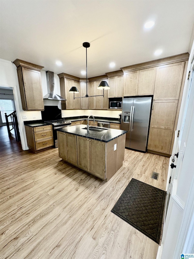 kitchen featuring sink, decorative light fixtures, appliances with stainless steel finishes, a kitchen island with sink, and wall chimney range hood