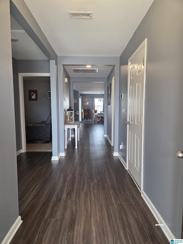 hallway with dark wood-type flooring, visible vents, and baseboards