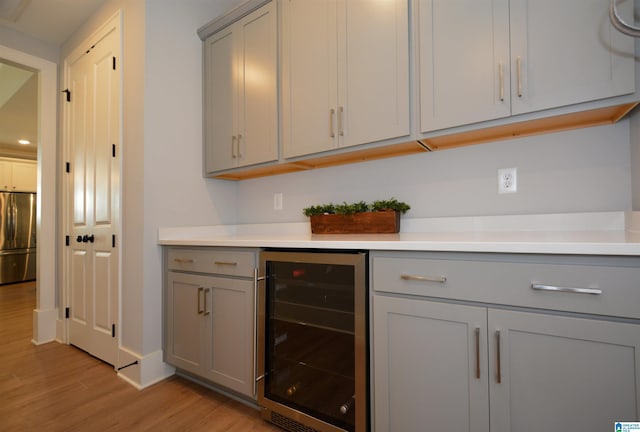 bar with a dry bar, light wood-style flooring, wine cooler, and stainless steel refrigerator