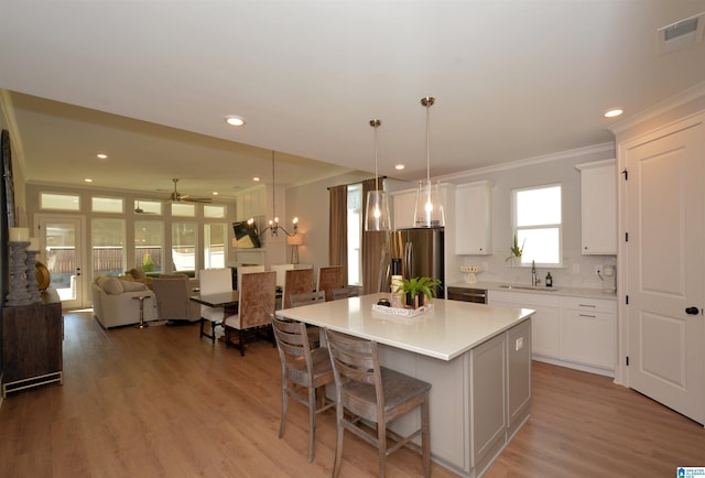 kitchen with a sink, white cabinetry, open floor plan, light countertops, and a center island