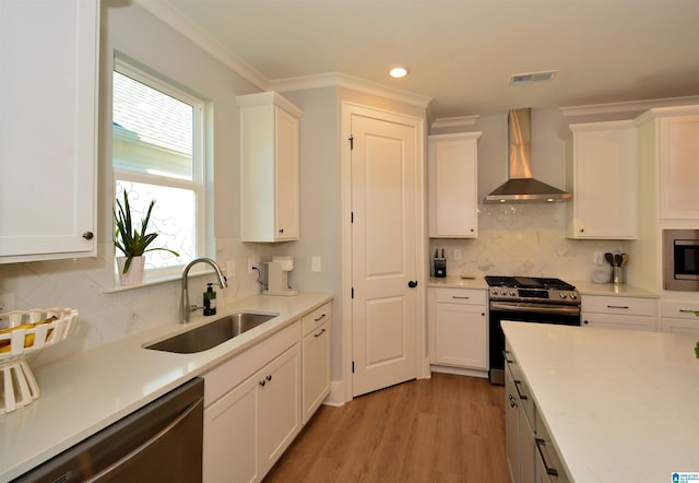 kitchen featuring light countertops, appliances with stainless steel finishes, white cabinetry, a sink, and wall chimney range hood