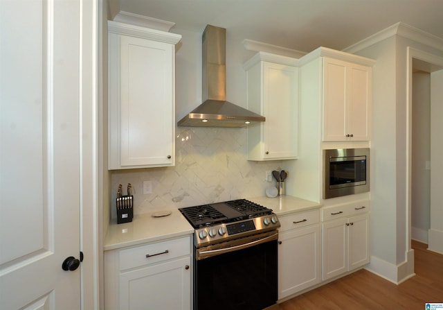 kitchen featuring white cabinetry, light countertops, wall chimney range hood, appliances with stainless steel finishes, and backsplash