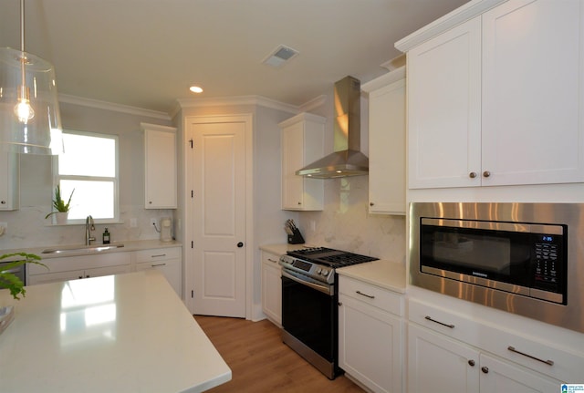 kitchen with light countertops, visible vents, appliances with stainless steel finishes, a sink, and wall chimney exhaust hood